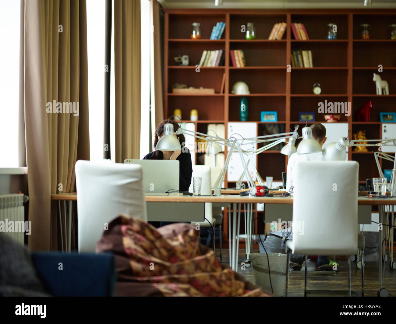 Un bureau avec lampe de travail en bois contre les grands meubles de bureau moderne avec chambre à l'intérieur dans des tons bruns Banque D'Images