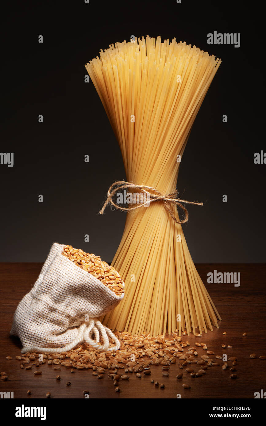 Les pâtes spaghetti sec attaché avec de la corde et sac de toile de grains de blé sur la table en bois sombre sur fond gris Banque D'Images