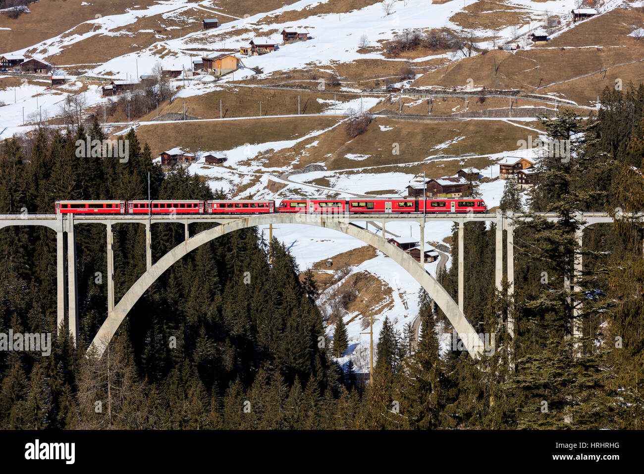Train rouge du chemin de fer rhétique sur Langwieser Viaduct entouré de bois, dans le canton des Grisons, Suisse Banque D'Images