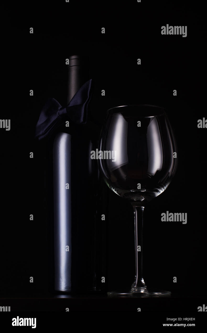 Vue de face vertical noir rouge bouteille de vin avec bouchon et aucune étiquette, grand verre vide et un noeud papillon noir sur le cou Banque D'Images