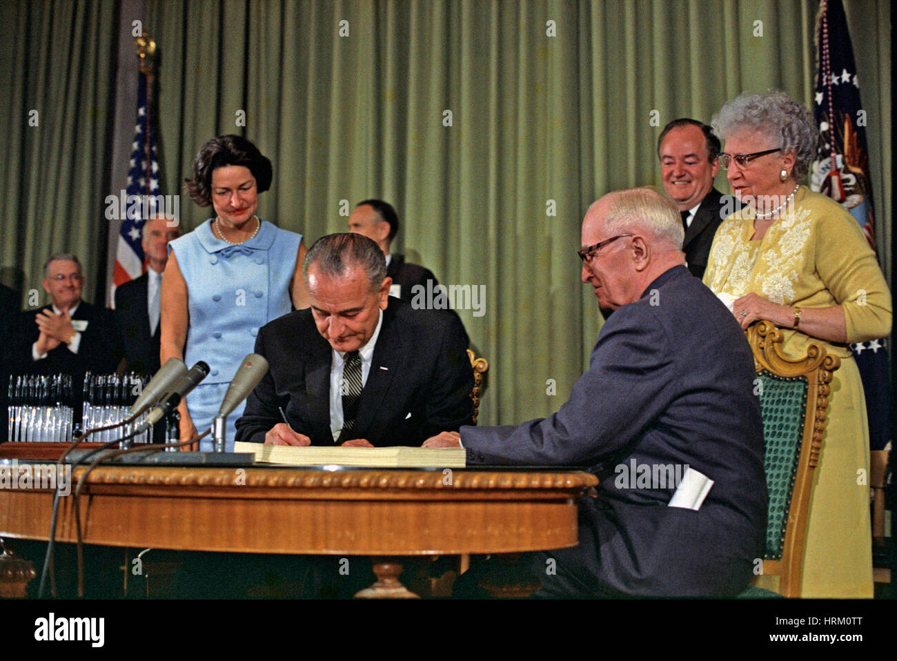 Le Président Lyndon B. Johnson signe la Loi sur l'assurance-maladie 30 Juillet 1965 suivi par son épouse Lady Bird en bleu et l'ancien président Harry S. Truman assis à droite avec sa femme Bess en jaune. Vice-Président Hubert Humphrey est à droite. Photo : officiel de la Maison Blanche Banque D'Images