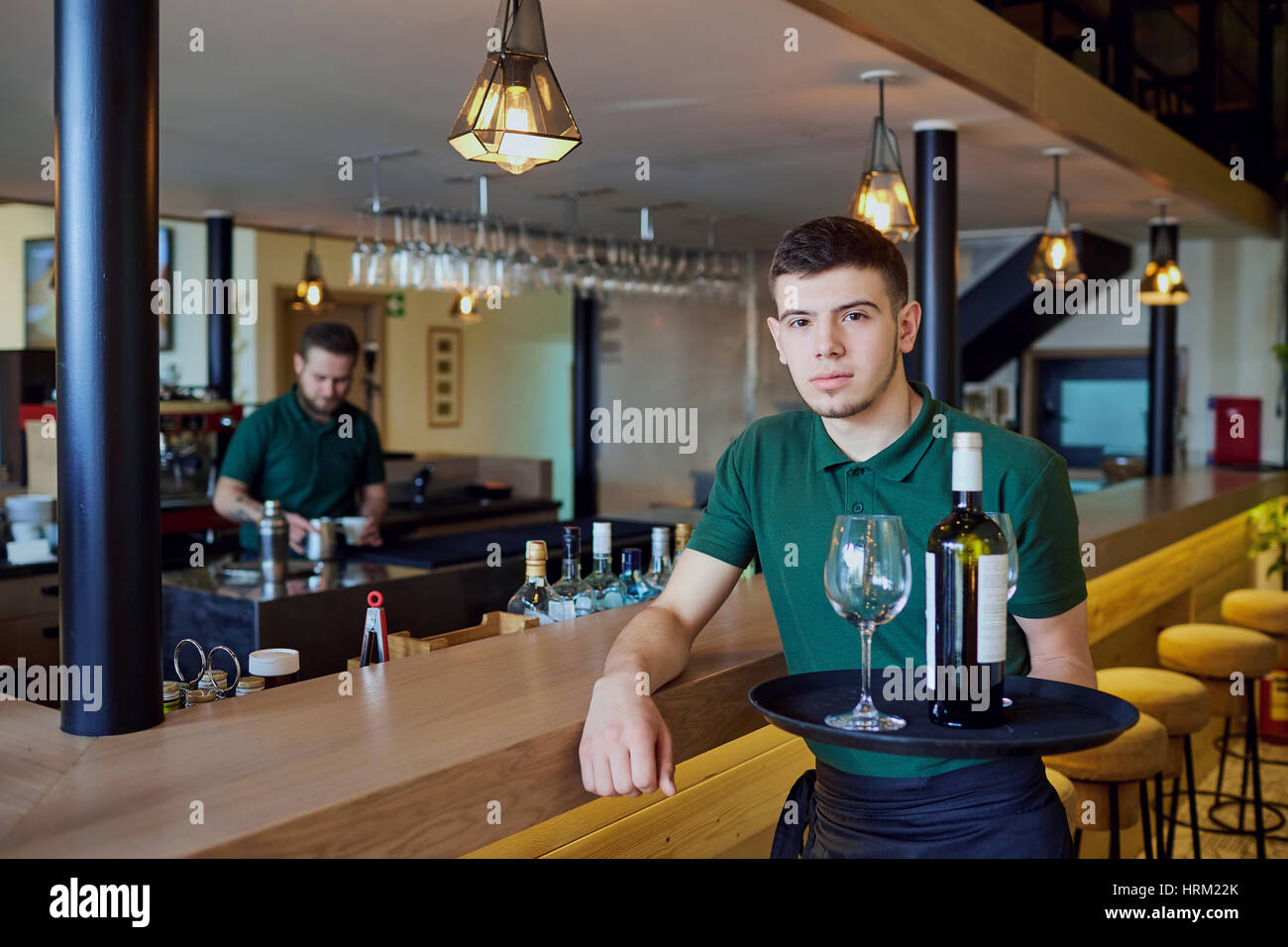 Un garçon tenant un plateau avec une bouteille de vin et des verres en bar Banque D'Images