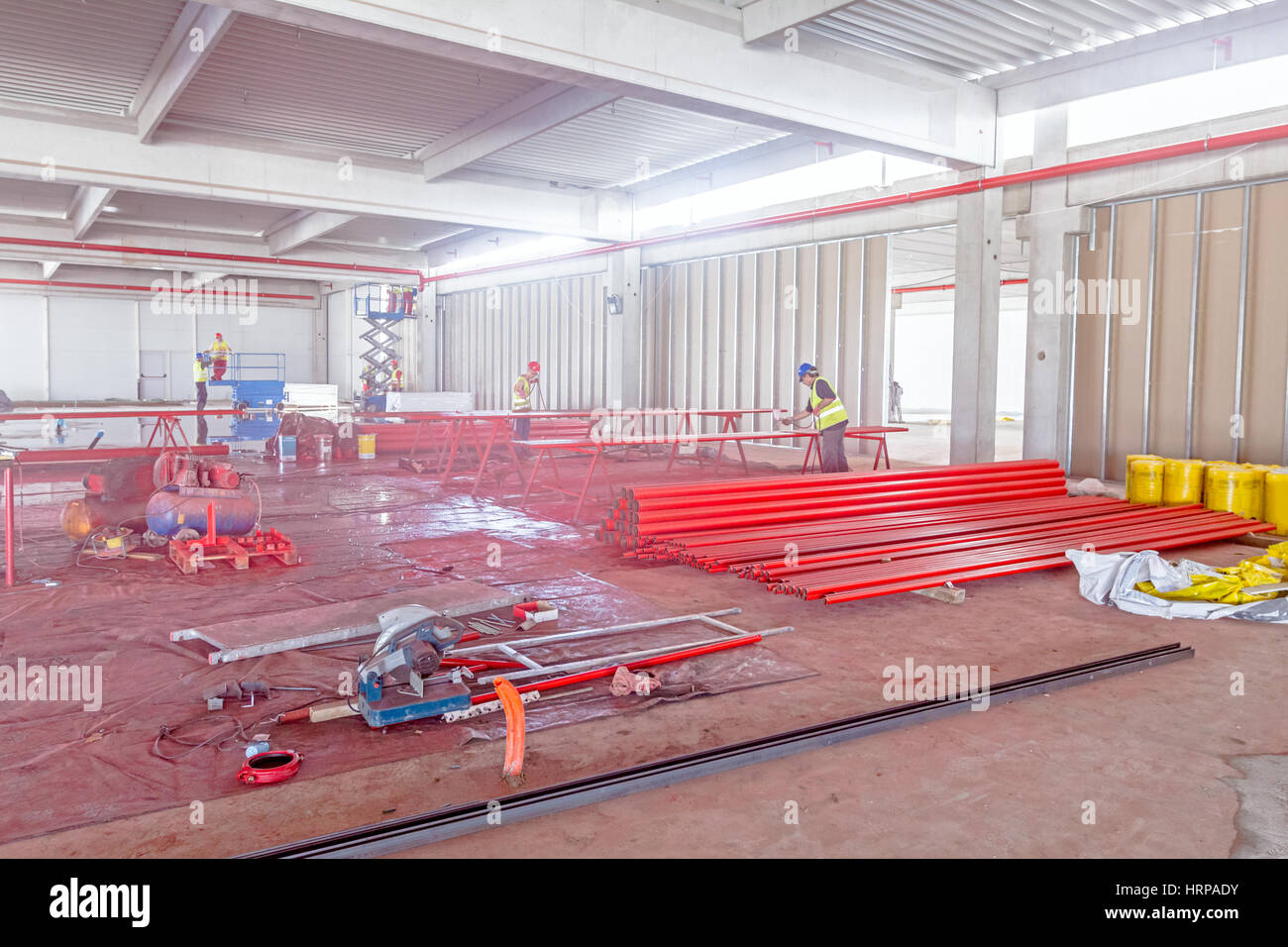 Les travailleurs sont rond long de la peinture rouge dans les tuyaux à l'aide d'un pistolet aérographe at construction site. Banque D'Images