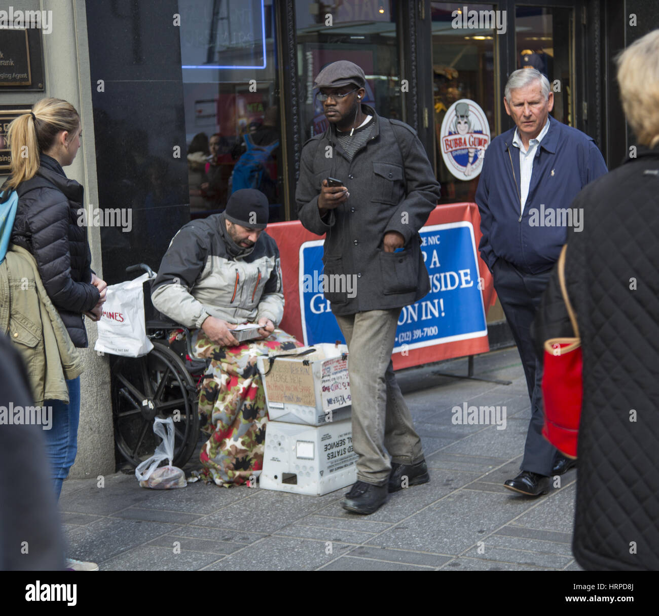 Sans-abri nous amène dans un wheelhair que le monde passe par le long de la 42e Rue dans Times Square, New York City. Banque D'Images