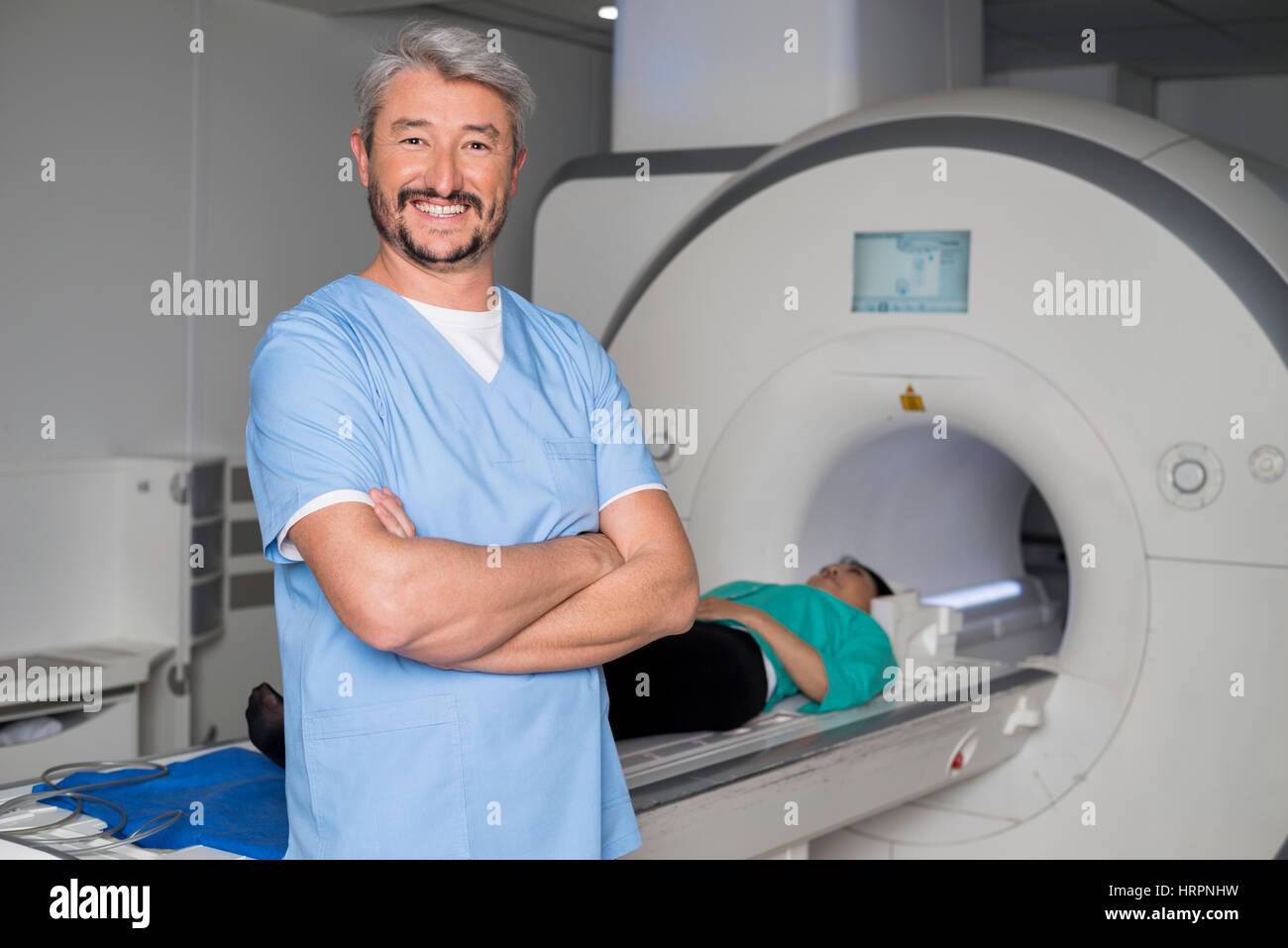 Portrait of happy young woman standing arms crossed avec patient couché sur irm à l'hôpital de la machine Banque D'Images