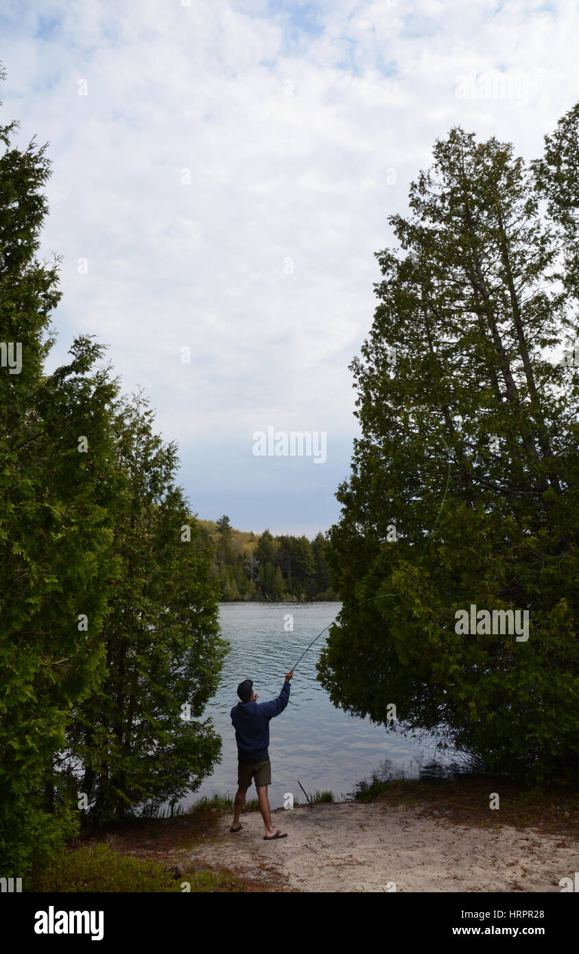 Un homme essaye la pêche à la mouche sur les rives d'un lac entre les deux arbres. Banque D'Images