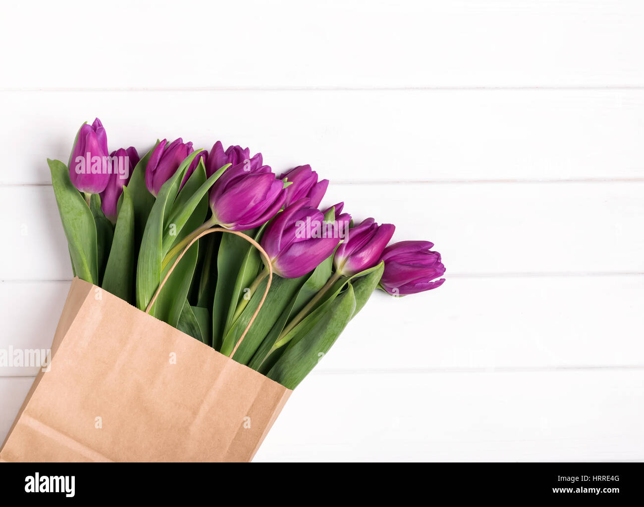 Tulipe rose dans un sac en papier sur la table en bois blanc, vue du dessus Banque D'Images