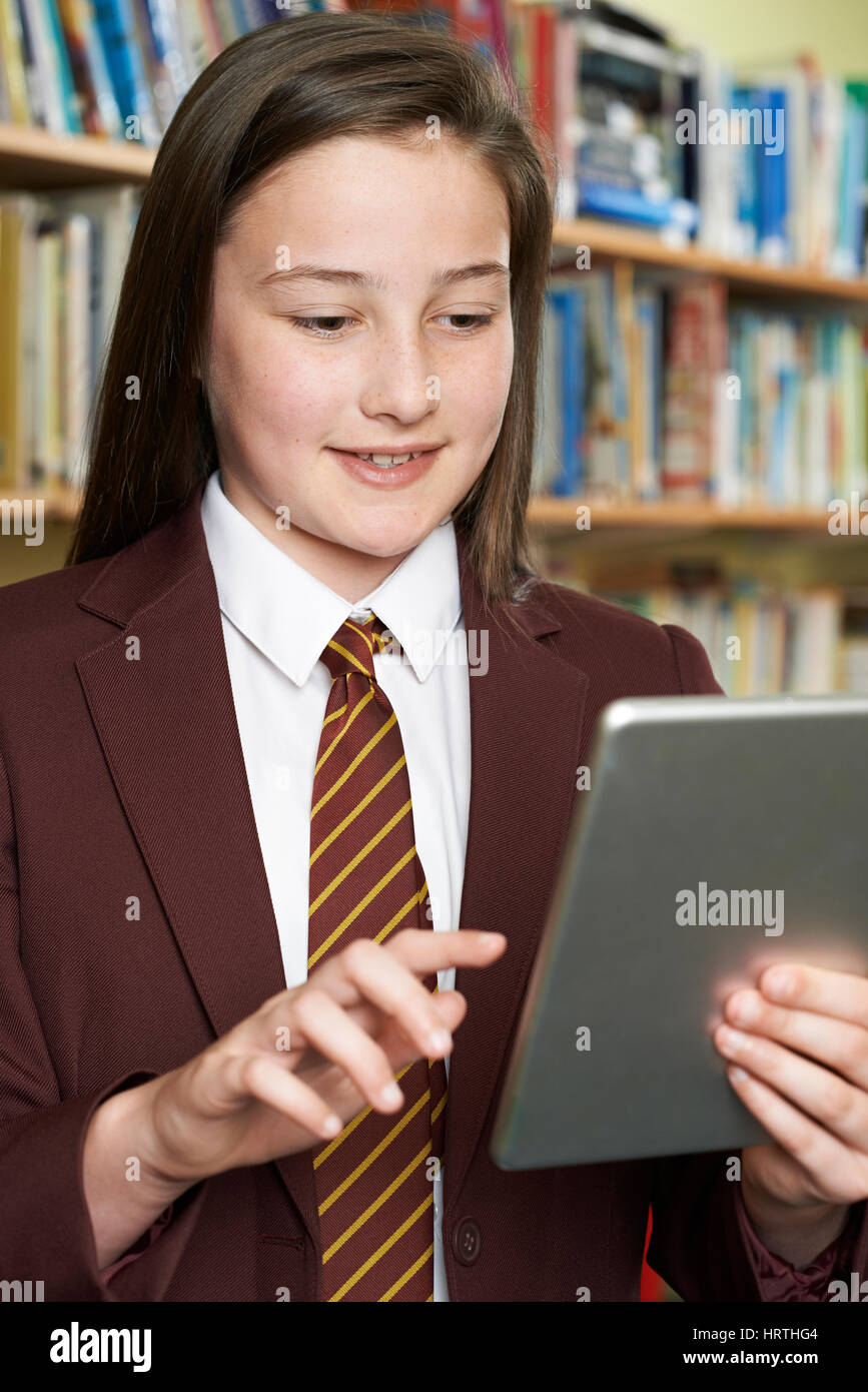 Girl Wearing School Uniform Using Digital Tablet In Library Banque D'Images