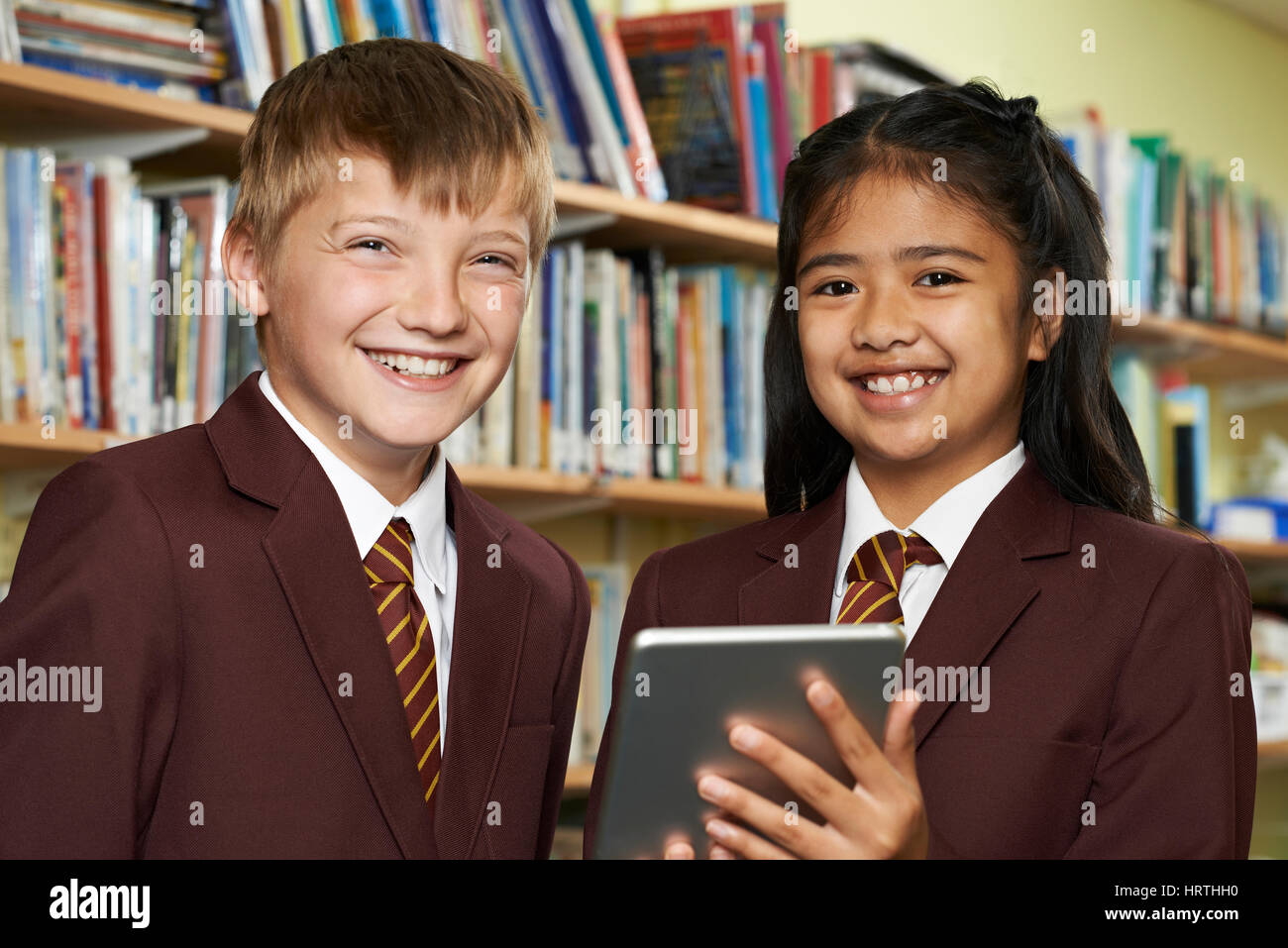 Portrait d'élèves portant des uniformes scolaires Using Digital Tablet In Library Banque D'Images