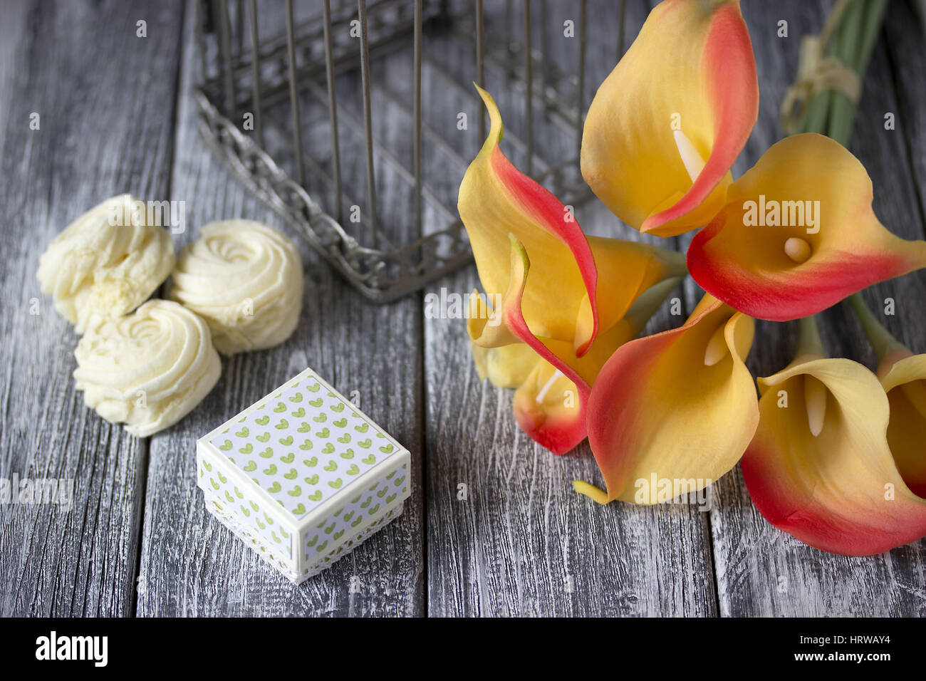 Bouquet de lis calla jaune orange avec de la guimauve et boîte en carton gris sur un fond de bois Banque D'Images