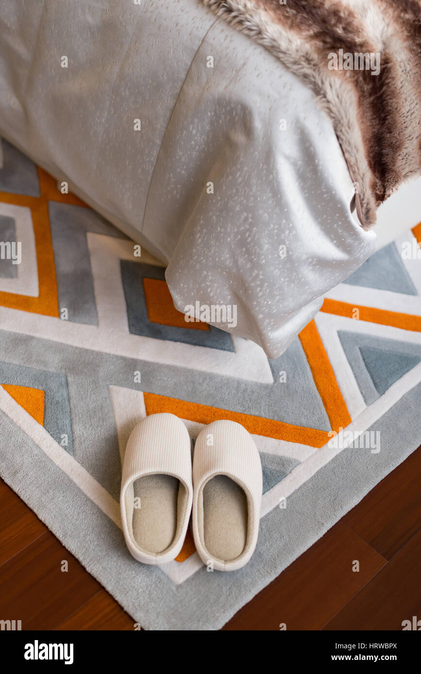 Paire de chaussons blanc sur un lit à proximité de tapis Banque D'Images