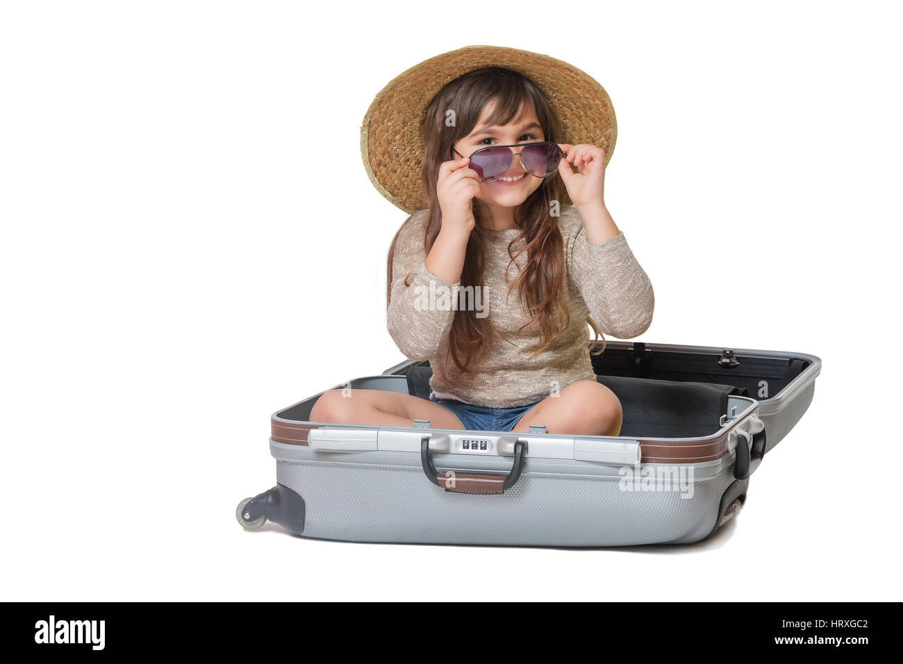 Portrait of smiling little girl touriste avec chapeau de paille sur la tête et lunettes tenant dans ses mains est assis dans la valise. Tout est sur le bac blanc Banque D'Images