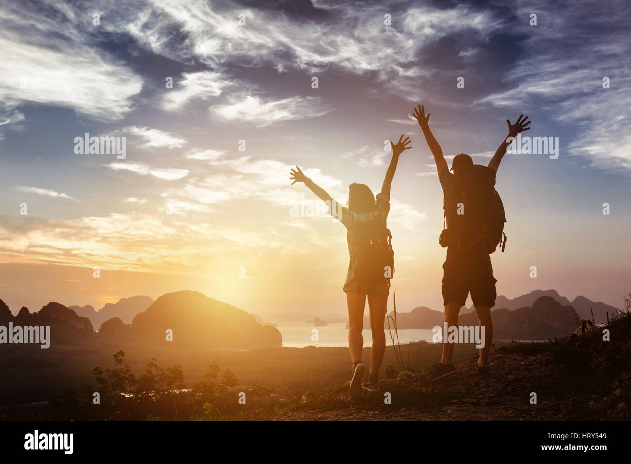 Couple heureux gagnant est levé posent avec bras sur fond de montagnes lever du soleil et de la mer. Concept de réussite Banque D'Images