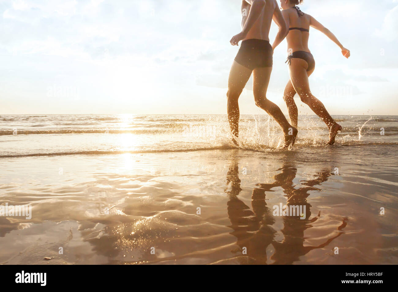 Happy young couple fonctionnant à la mer sur la plage au coucher du soleil, les silhouettes de l'homme et de la femme, des vacances en famille Banque D'Images