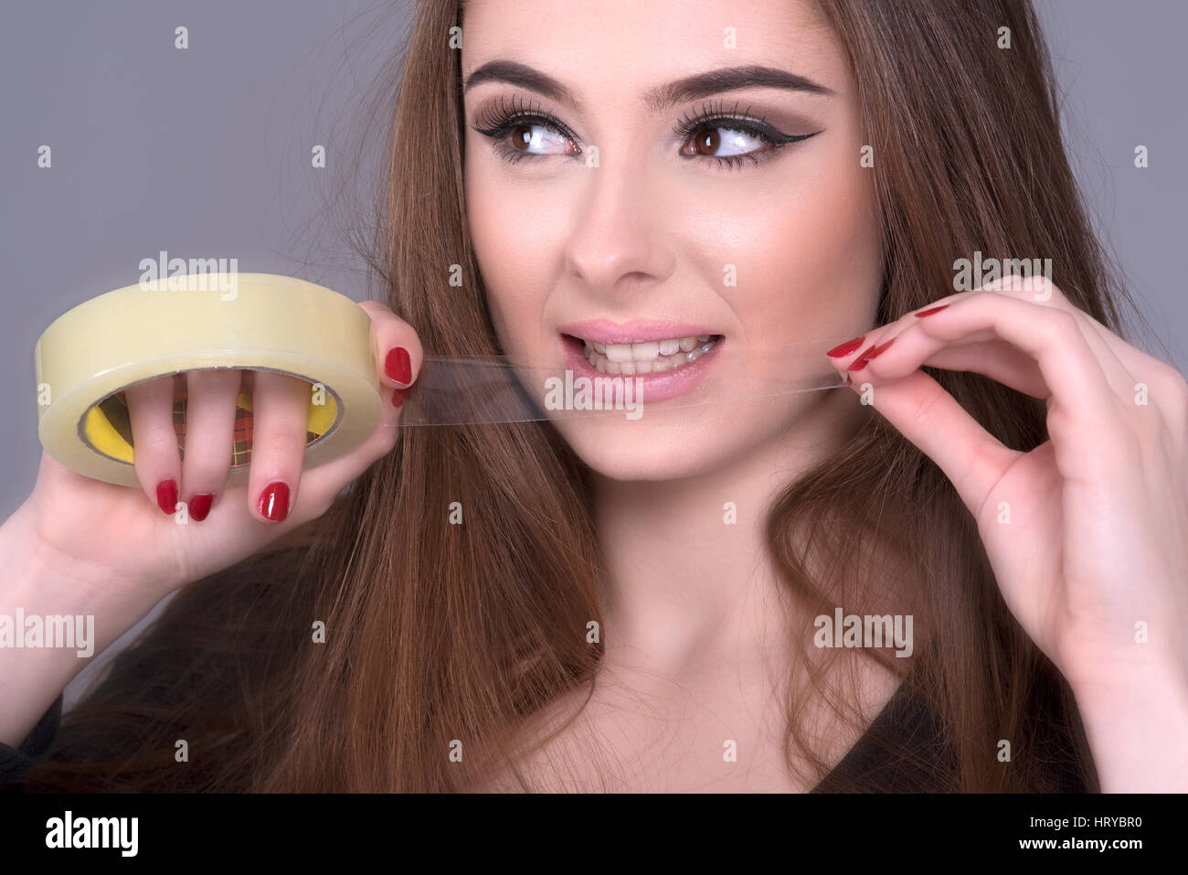 Femme déchirant un longueur de ruban gommé sur un rouleau avec ses dents Banque D'Images