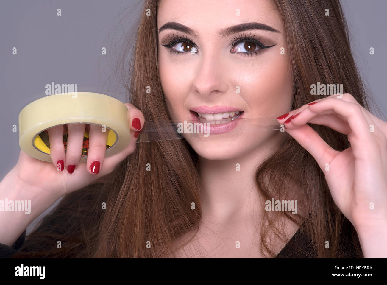 Femme déchirant un longueur de ruban gommé sur un rouleau avec ses dents Banque D'Images