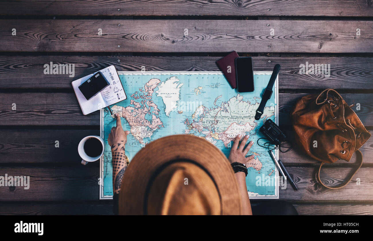 Tourist pointant sur l'Alaska sur la carte du monde avec ses accessoires de voyage autour. Jeune femme portant chapeau brun la planification d'un tour en regardant le monde ma Banque D'Images