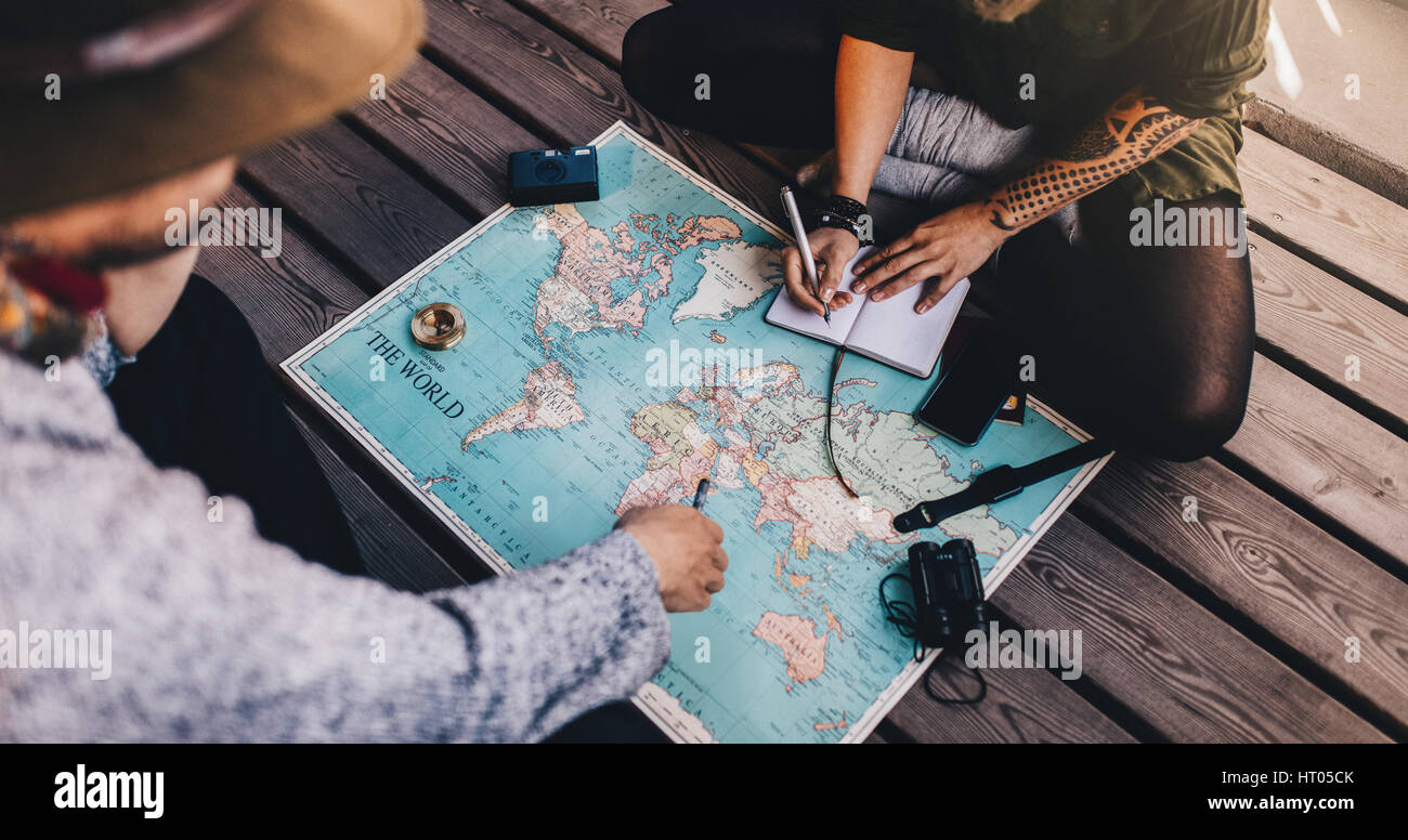 L'homme et la femme à l'aide d'une visite de planification carte du monde. Femme de prendre des notes pendant que l'homme est dirigé vers la carte du monde des accessoires de voyage autour. Banque D'Images