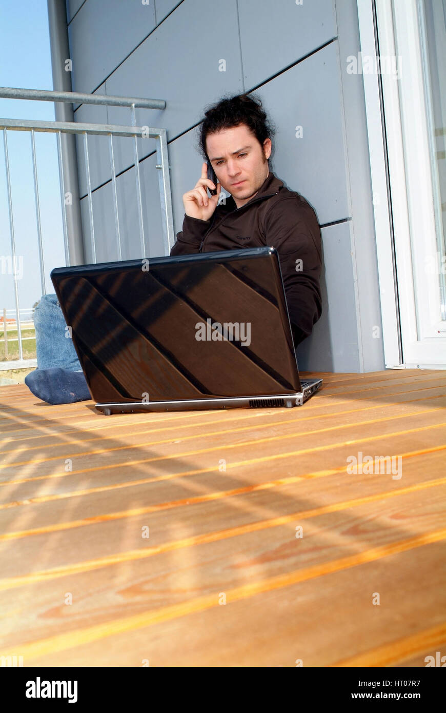 Junger Mann sitzt am sonnigen und arbeitet suis Notebook - jeune homme assis sur le balcon ensoleillé et using laptop Banque D'Images