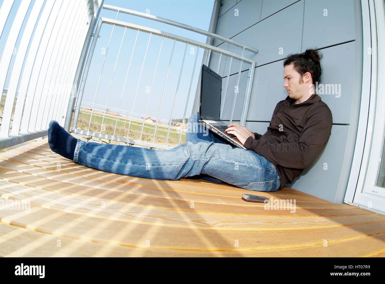 Junger Mann sitzt am sonnigen und arbeitet suis Notebook - jeune homme assis sur le balcon ensoleillé et using laptop Banque D'Images