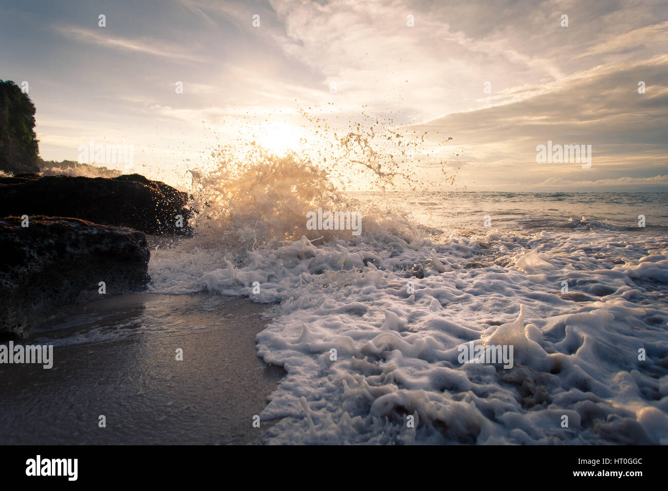 Océan vagues avec mousse de battre contre les rochers au coucher du soleil. Le magnifique paysage de la puissance élémentaire de l'eau. Bali Indonésie Banque D'Images