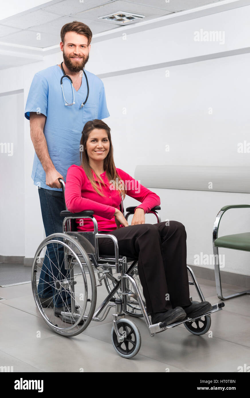 Portrait of smiling female patient assis en fauteuil roulant alors qu'infirmier debout derrière à l'hôpital Banque D'Images