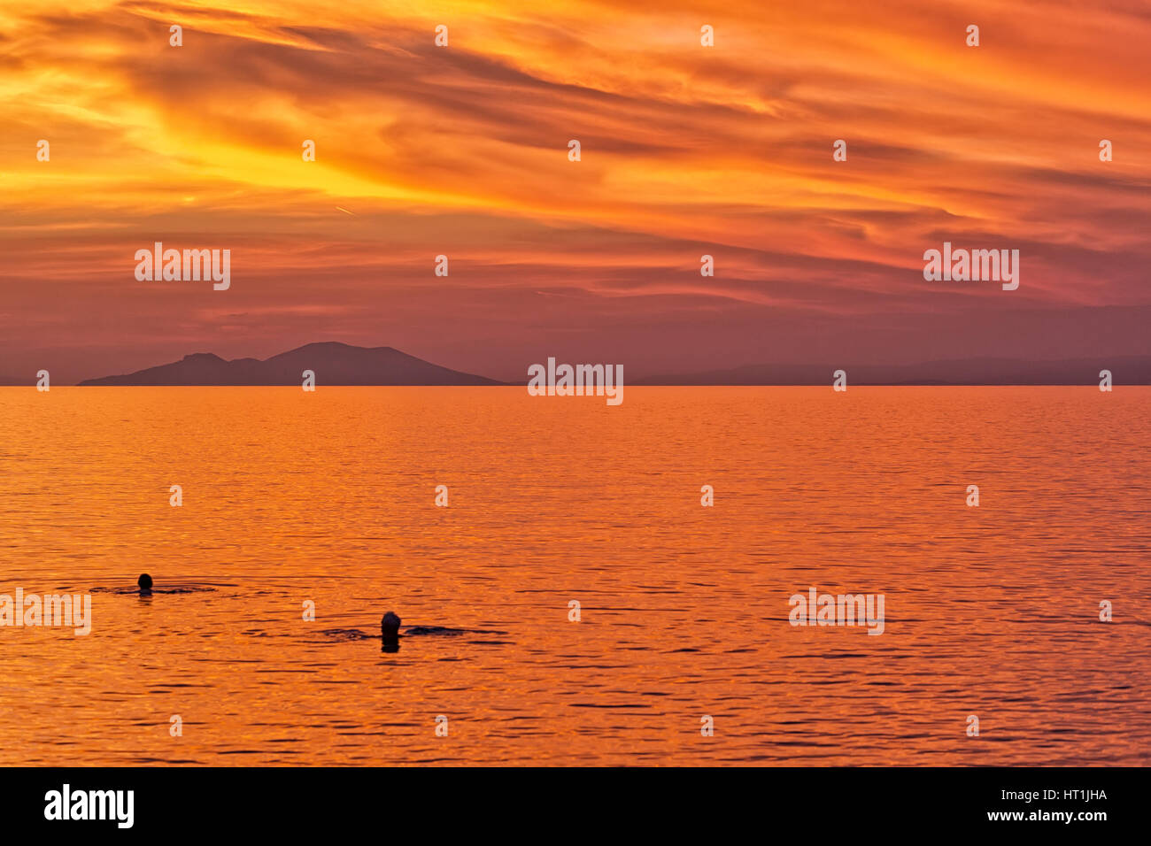 Silhouette d'un couple nageant dans la mer sur la toile de fond le coucher de soleil sur une plage avec belle orange et rouge ciel dramatique. Banque D'Images