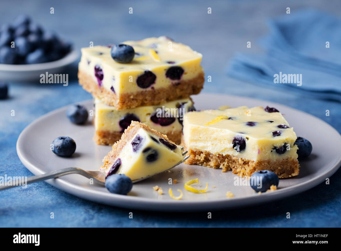 Barres aux bleuets, gâteau, gâteau au fromage sur une plaque gris sur fond noir en bleu Banque D'Images