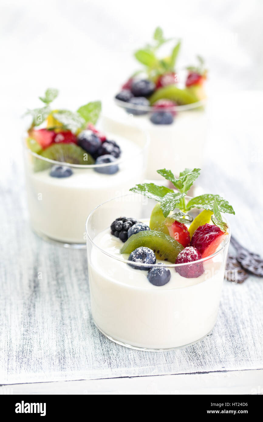 Yaourt frais aux fruits rouges. On white table rustique. Se concentrer sur les feuilles de menthe et de bleuet et de kiwis dans le centre du premier verre. Banque D'Images