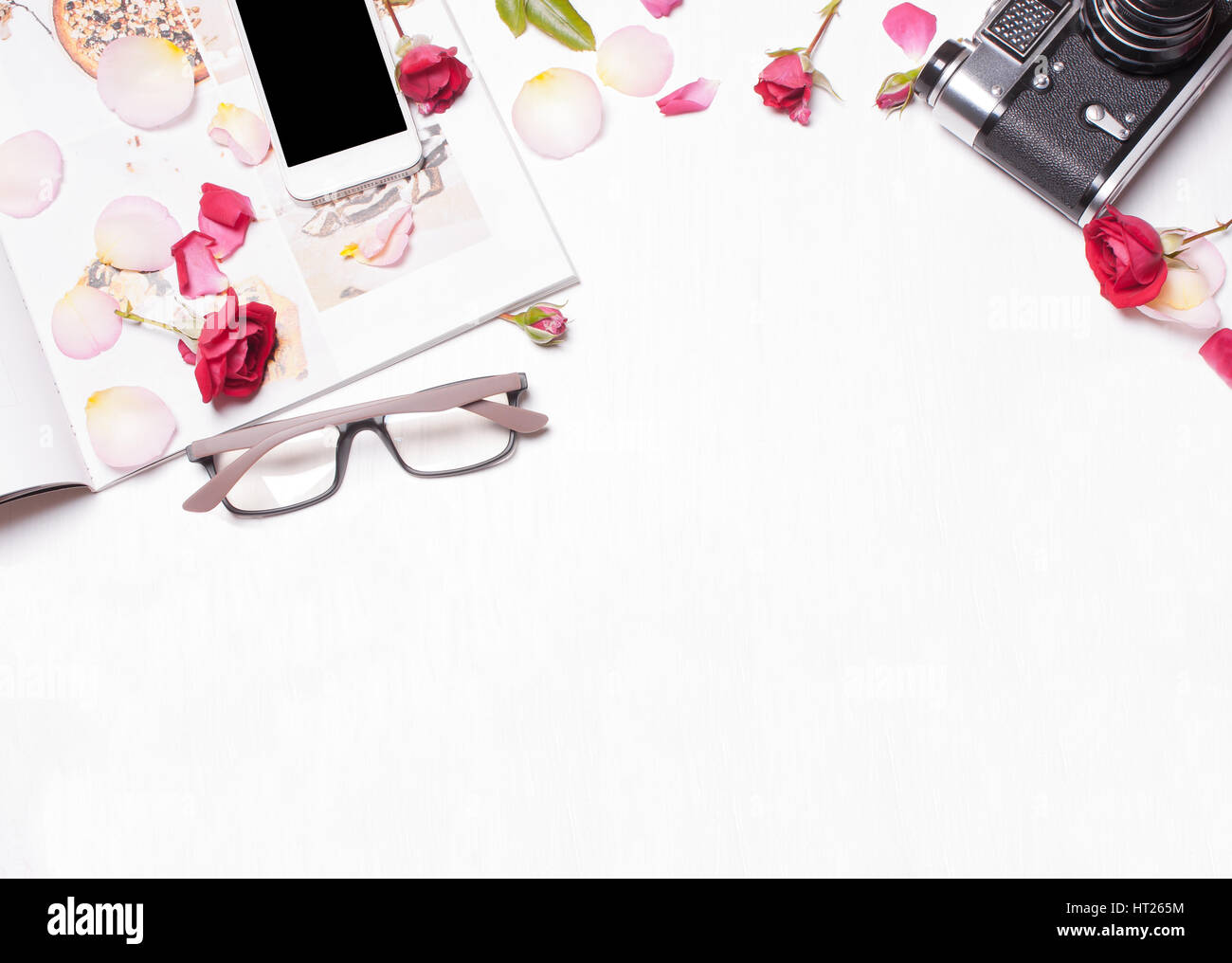 La composition de roses rouges, pétales, magazine, téléphone, appareil photo sur un fond blanc. Soft focus. Vue de dessus. L'espace de travail de créateur, crea concept Banque D'Images