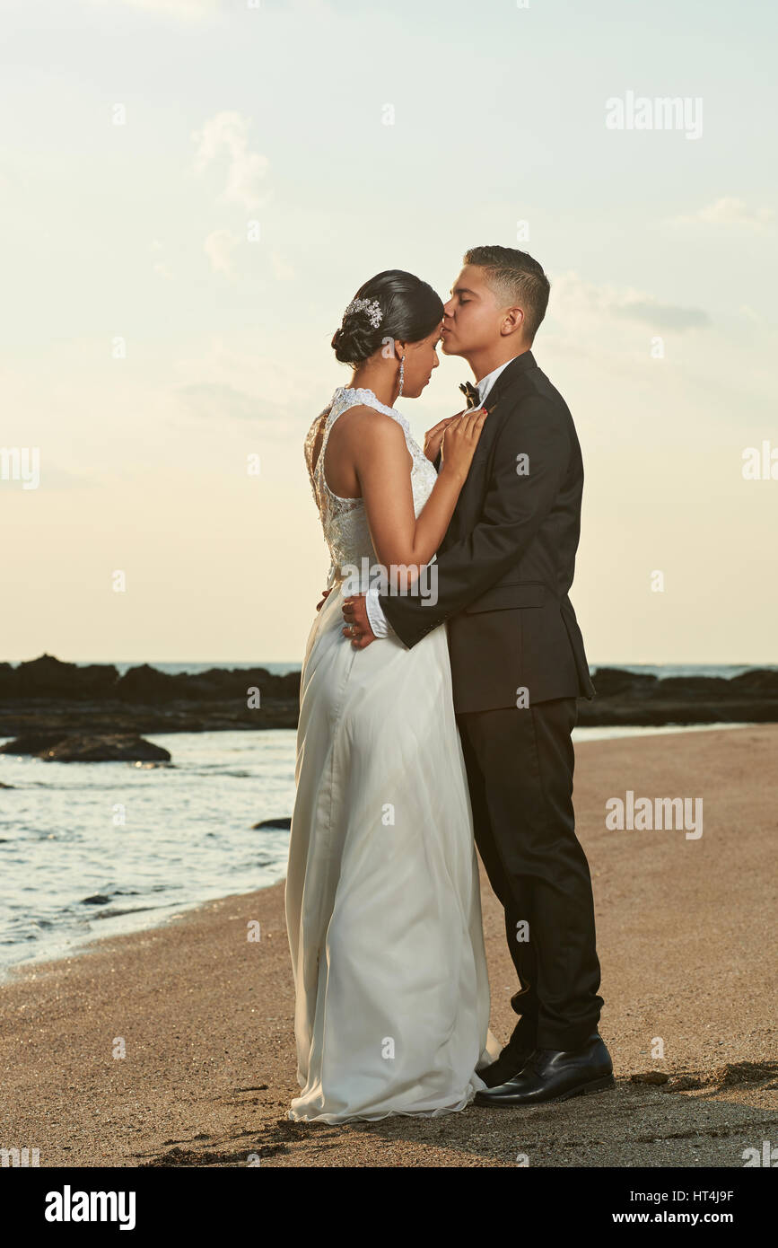 Hispanic couple de jeunes mariés sur le jour du mariage. Hugging Bride and Groom sur Ocean Beach Sunset Banque D'Images Hispanic couple de jeunes mariés sur le jour du mariage. Hugging Bride and Groom sur Ocean Beach Sunset Banque D'Images