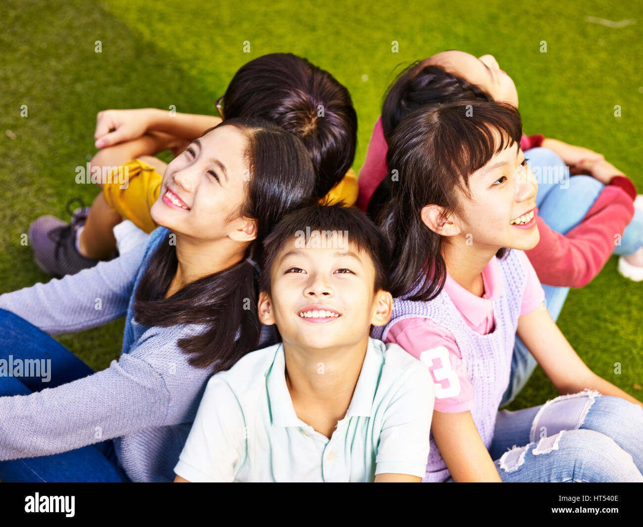 De l'école élémentaire du groupe asiatique filles et garçons assis sur l'herbe à aire le ciel Banque D'Images