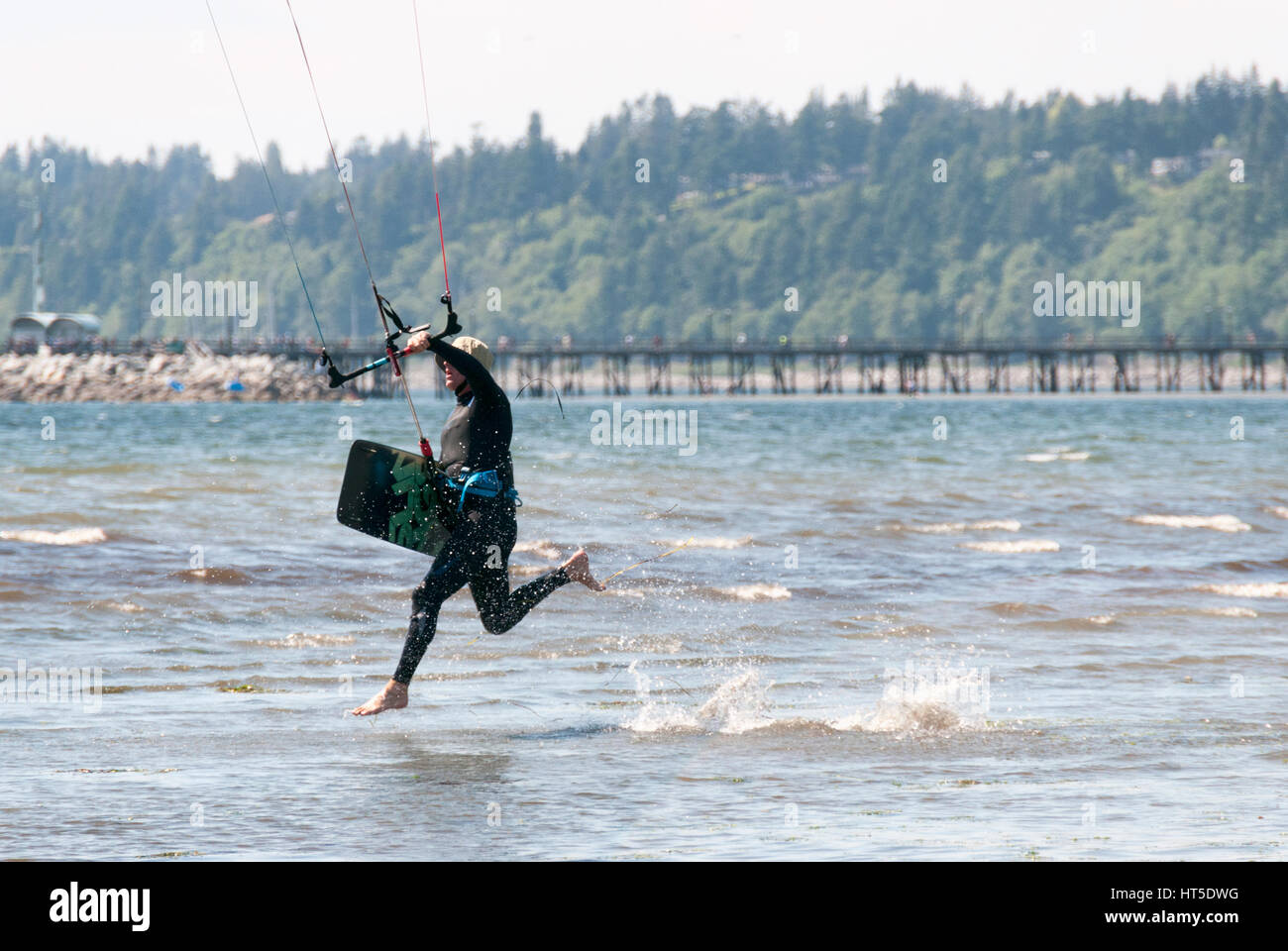 Dans l'homme qui court sur une plage de surf avec kitesurf board en main portant une combinaison de plongée. Banque D'Images