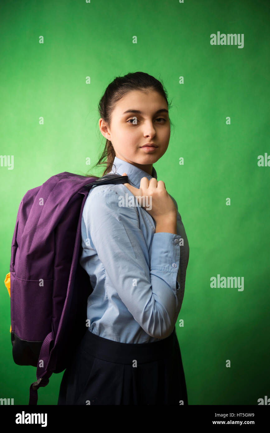 Une teen lycéenne en chemise bleue est debout avec un sac à dos violet sur ses épaules sur un arrière-plan chroma key vert Banque D'Images