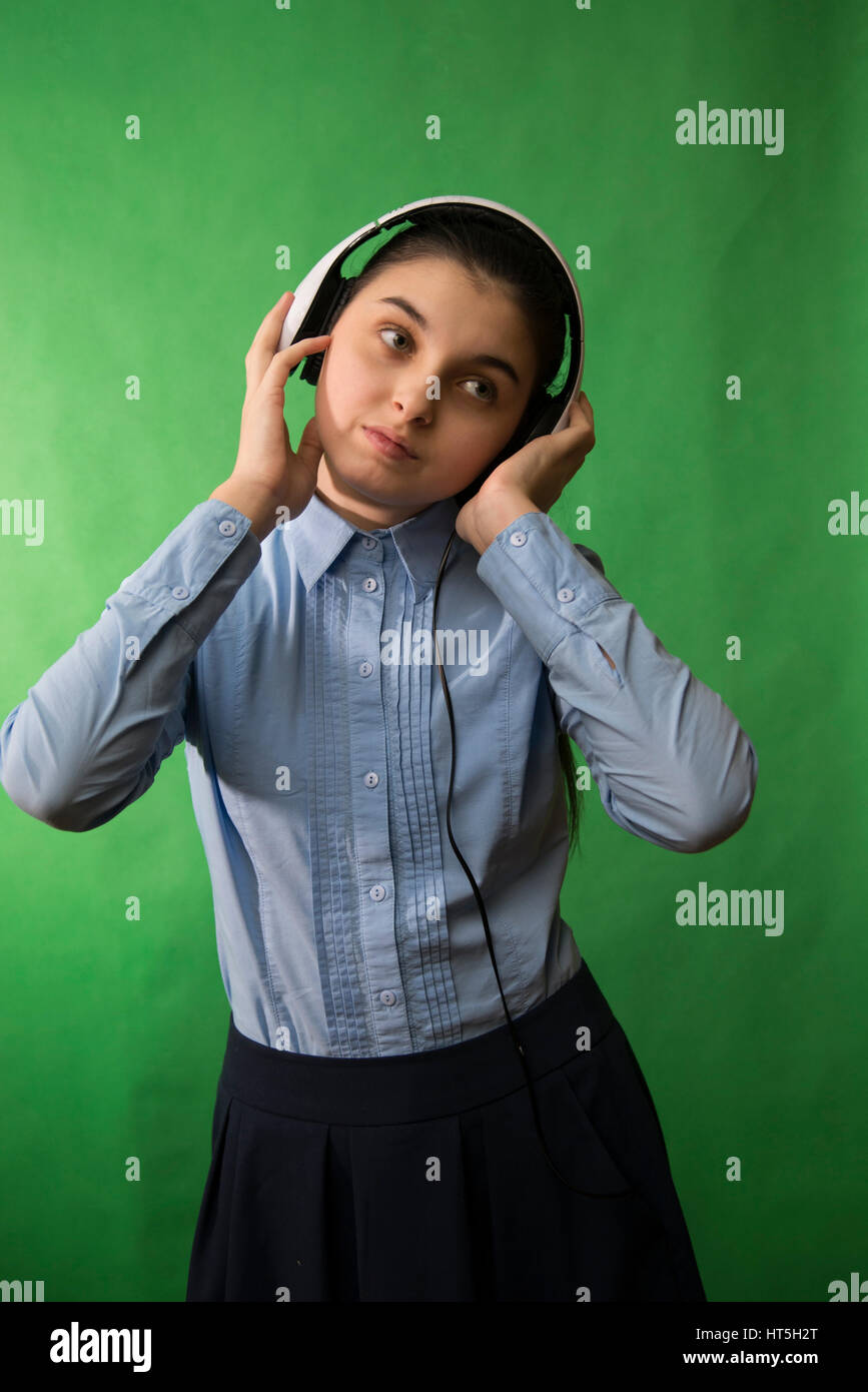 Teen lycéenne en chemise bleue est à l'écoute de la musique au casque blanc sur fond vert Banque D'Images