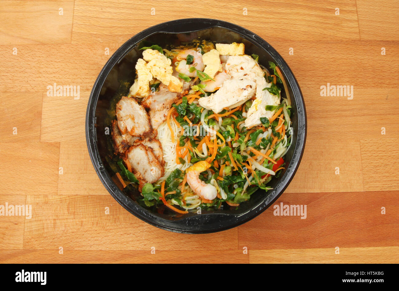 Four micro-ondes, repas chinois Singapour nouilles, dans un emballage en plastique sur un plan de travail de cuisine en bois Banque D'Images