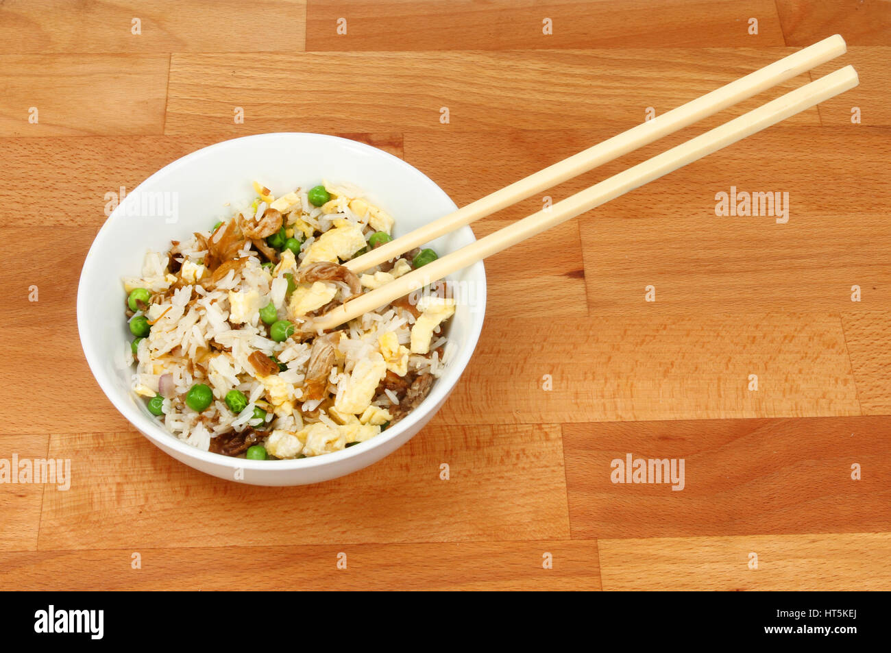 Riz frit avec des baguettes dans un bol sur un plan de travail de cuisine en bois Banque D'Images