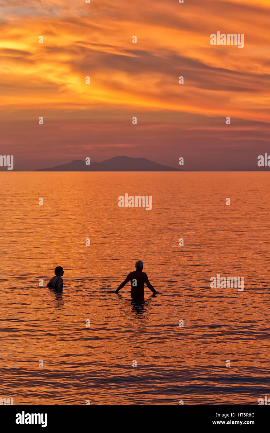 Silhouette d'un couple nageant dans la mer sur la toile de fond le coucher de soleil sur une plage avec belle orange et rouge ciel dramatique. Banque D'Images