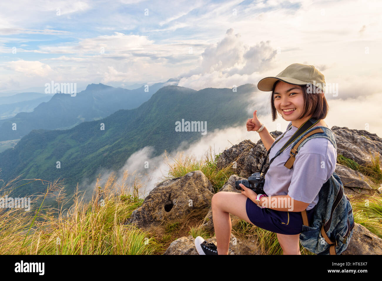 Superbdevotie asian cute teens fille avec appareil photo DSLR caps et son sac à dos se pose souriante pouce vers le haut sur le dessus de la montagne vue à Phu Chi Fa Banque D'Images