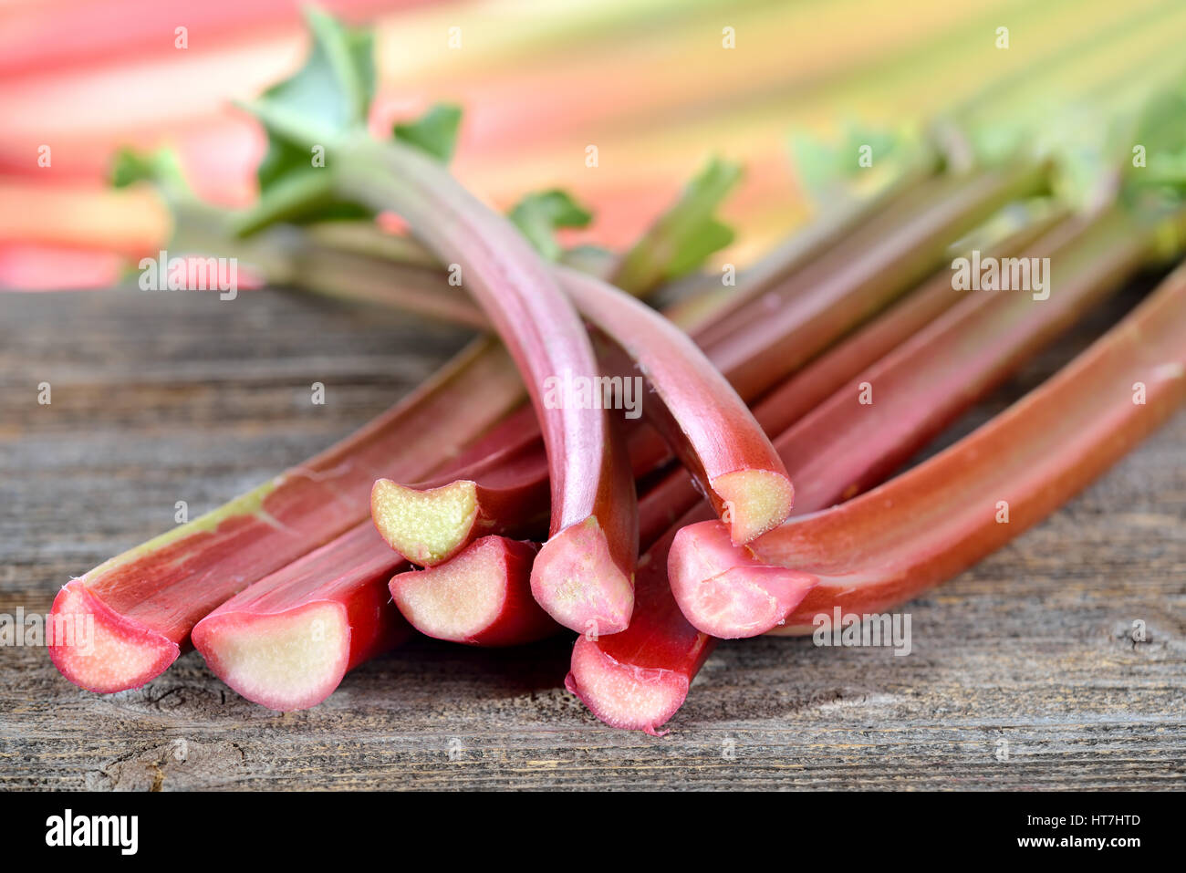 Rhubarbe fraîche sur une table en bois, dans l'arrière-plan d'autres tiges de rhubarbe dans soft focus Banque D'Images