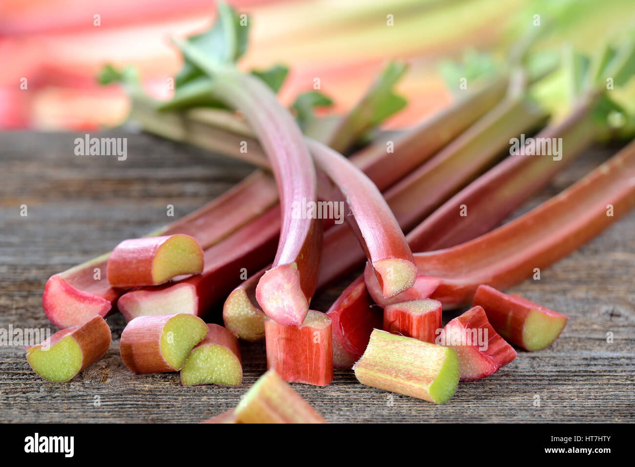 Rhubarbe fraîche sur une table en bois, dans l'arrière-plan d'autres tiges de rhubarbe dans soft focus Banque D'Images
