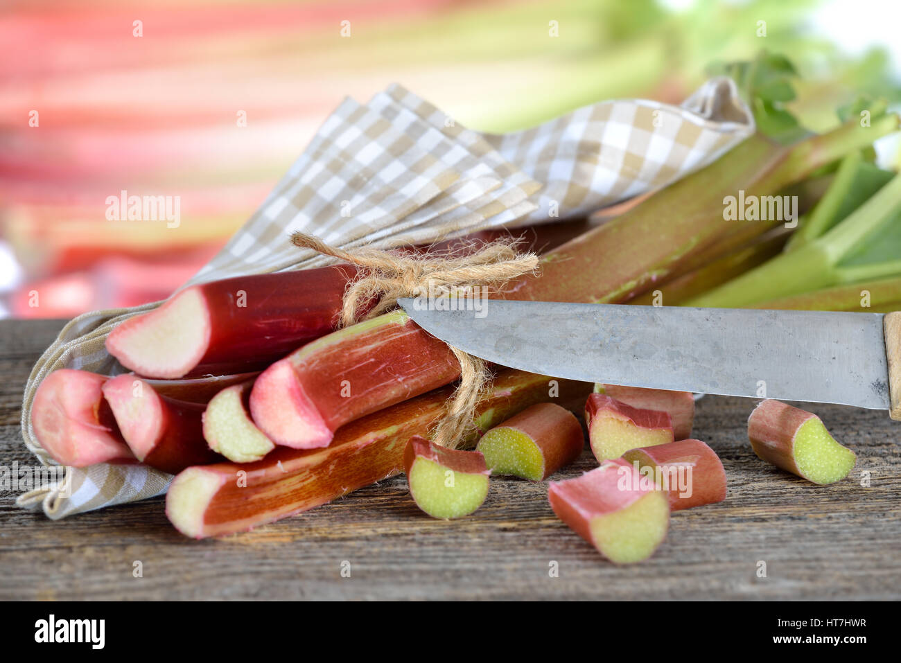 Rhubarbe fraîche sur une table en bois avec un vieux couteau de chef, dans l'arrière-plan d'autres tiges de rhubarbe dans soft focus Banque D'Images