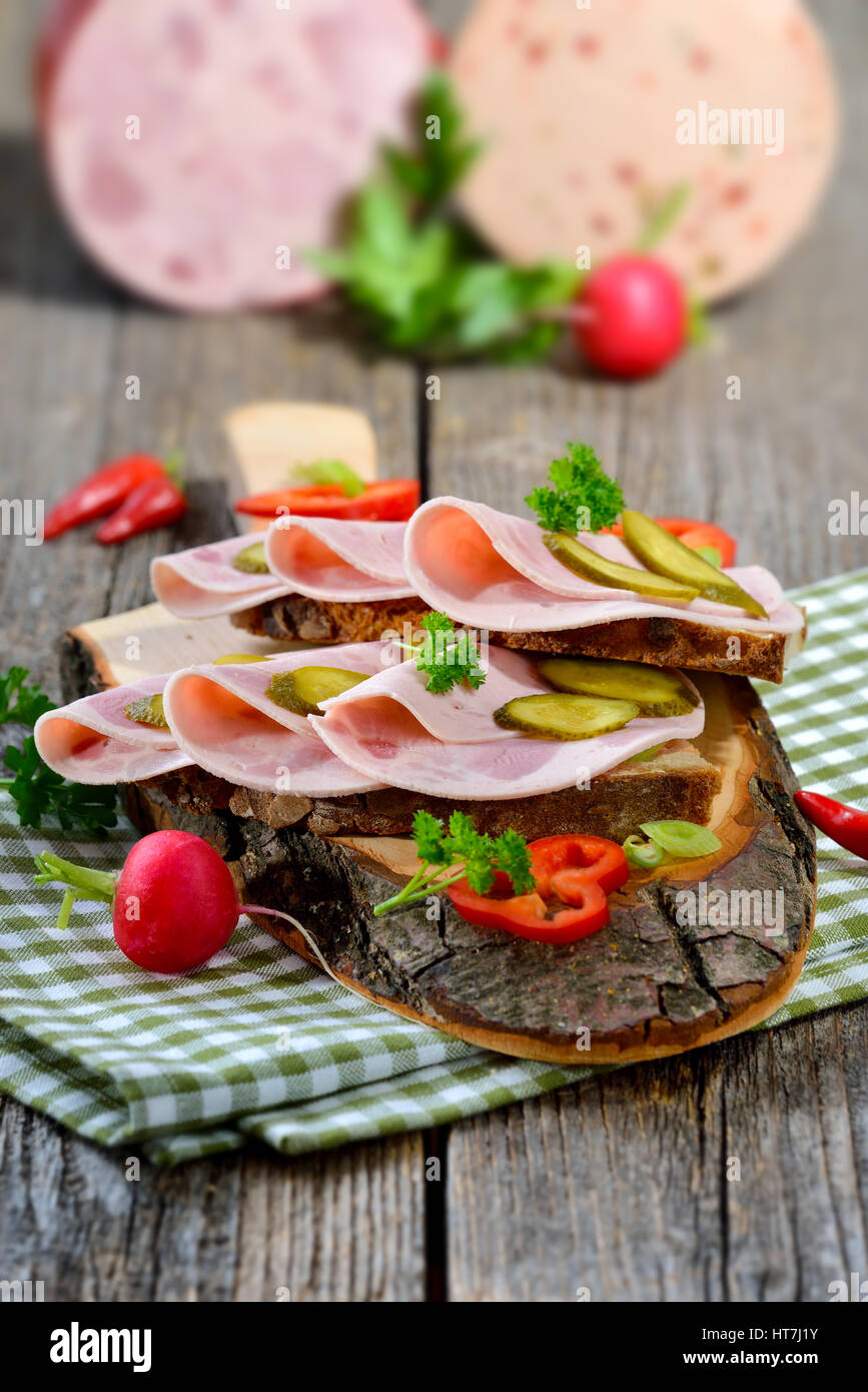 Tranches de saucisse Bavaroise sur pain de campagne, garni et servi sur une planche en bois rustique Banque D'Images