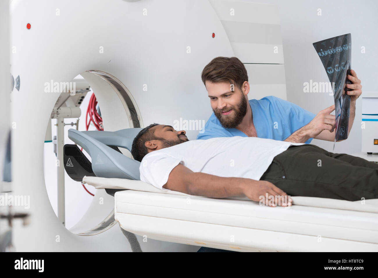 Jeune médecin homme montrant x-ray à patient couché sur scanner à l'hôpital Banque D'Images
