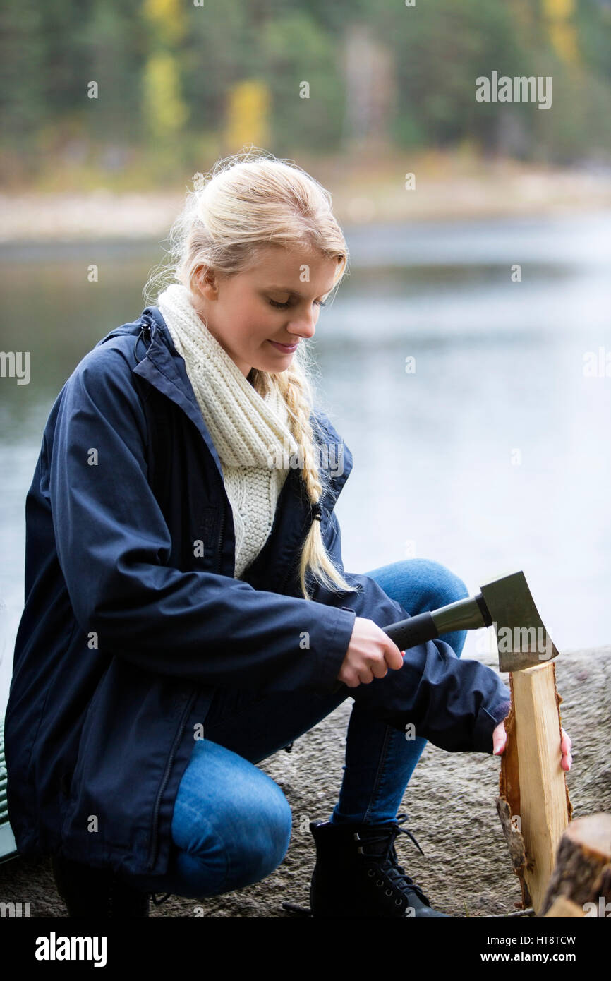 Jeune femme la coupe de bois de feu sur le camping au bord du lac Banque D'Images