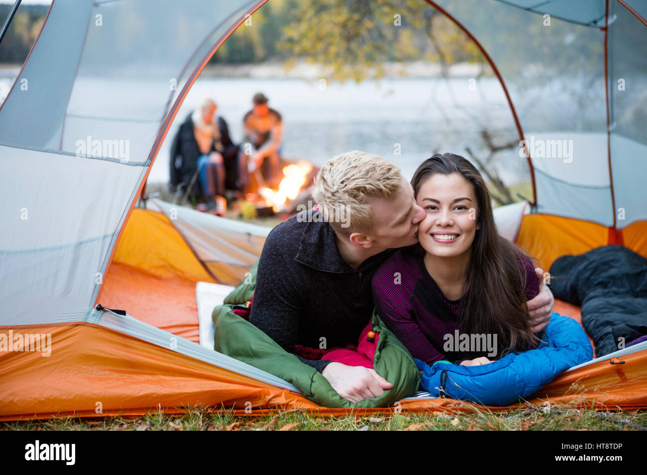 Jeune homme femme s'embrasser tout en se trouvant dans une tente avec des amis en arrière-plan au Lakeshore Banque D'Images