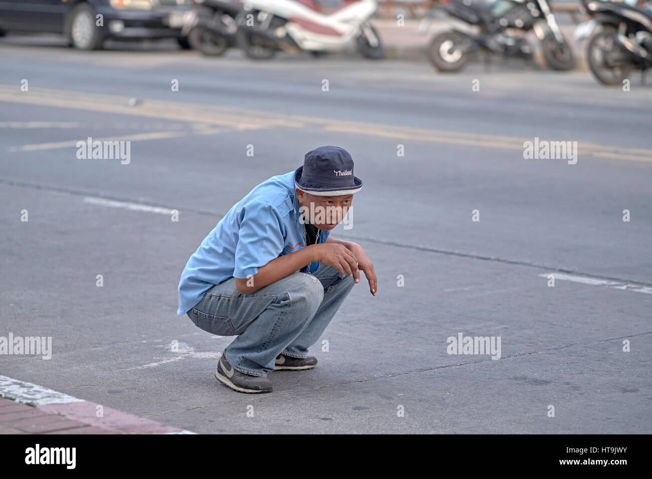 L'homme accroupi pour inspecter le dessous de sa voiture pour une fuite de liquide suspect. La Thaïlande en Asie du sud-est. Banque D'Images