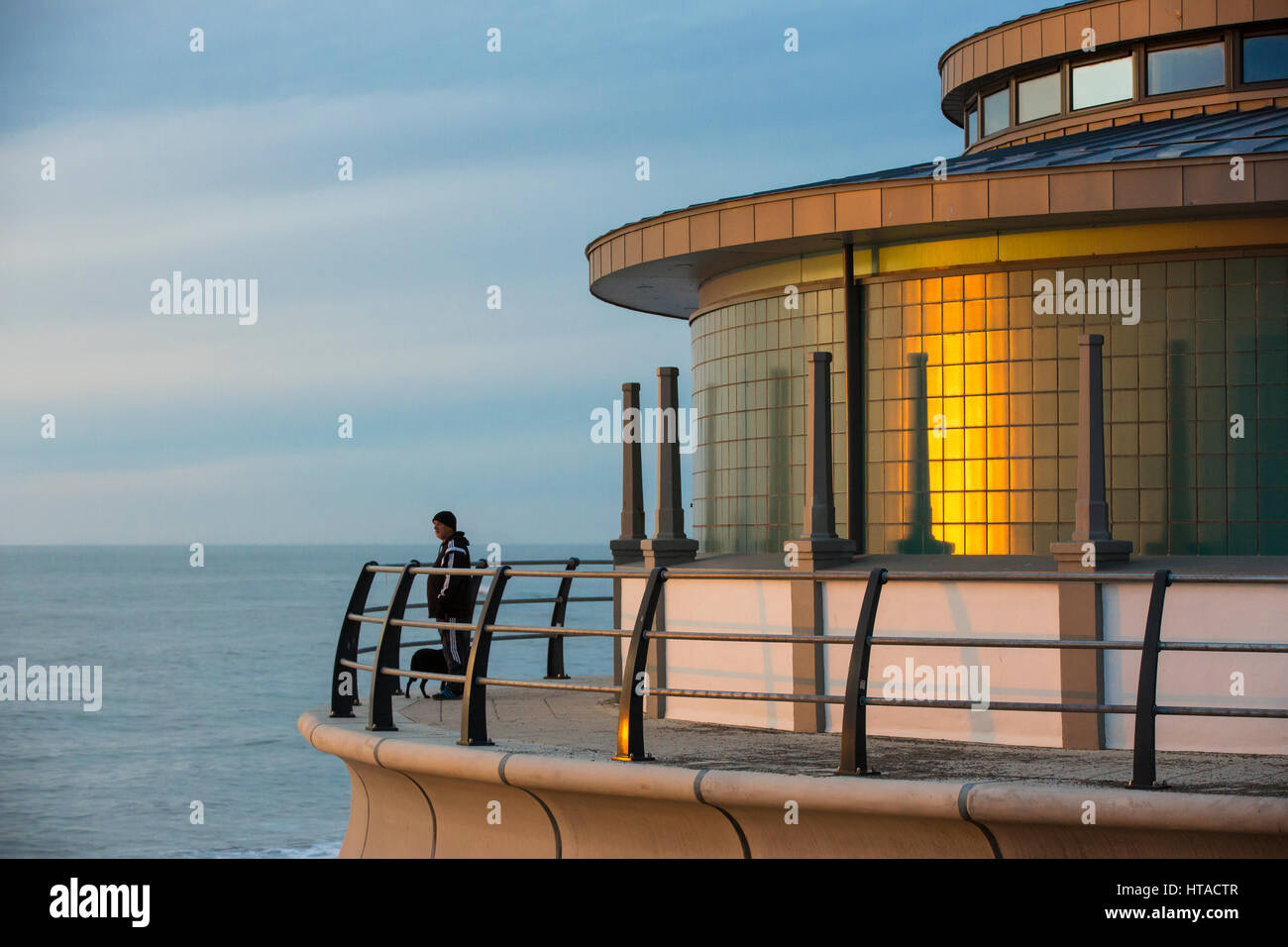 Aberystwyth, Pays de Galles, Royaume-Uni. 9 mars 2017. Un homme avec un chien regarde le coucher de soleil depuis le front de kiosque à musique, avec la lumière du soleil couchant reflété sur ses murs. Credit : Alan Hale/Alamy Live News Banque D'Images