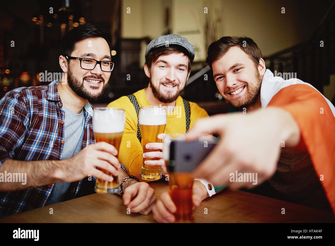 Trois hommes barbus souriants posant avec de grands verres à shot selfies table ronde au Sports Bar Banque D'Images