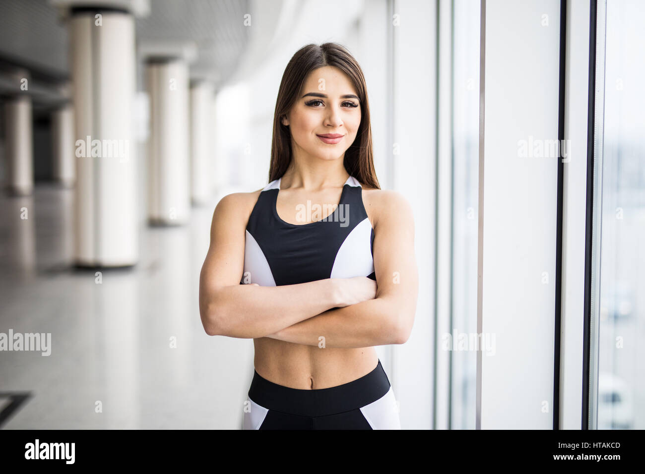 Femme avec les mains croisées dans les vêtements de sport à la caméra à tout en se tenant devant de la fenêtre à la salle de sport Banque D'Images